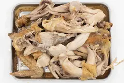 Eight pieces of a carved chicken including two carcass halves, two breasts, two wings, and two thighs on a baking pan.