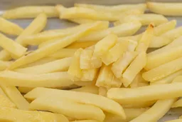 Ten pieces of broken-up baked french fries are stacked on top of pieces of whole fries on a grooved silver baking pan.
