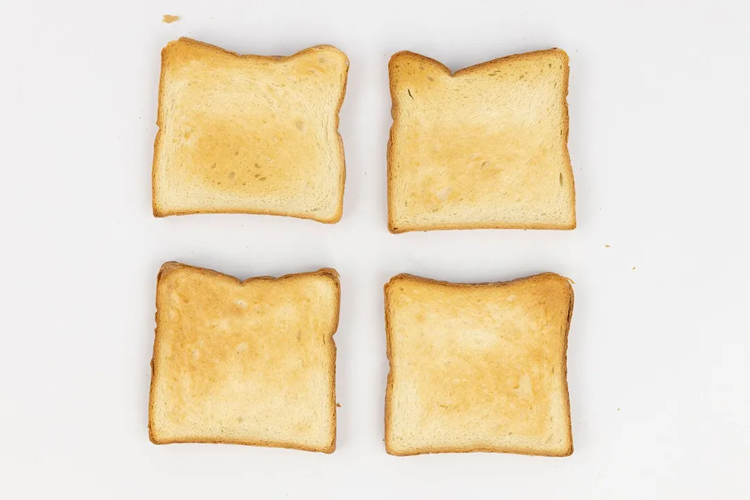 Four pieces of golden brown toast by a toaster oven on a white background