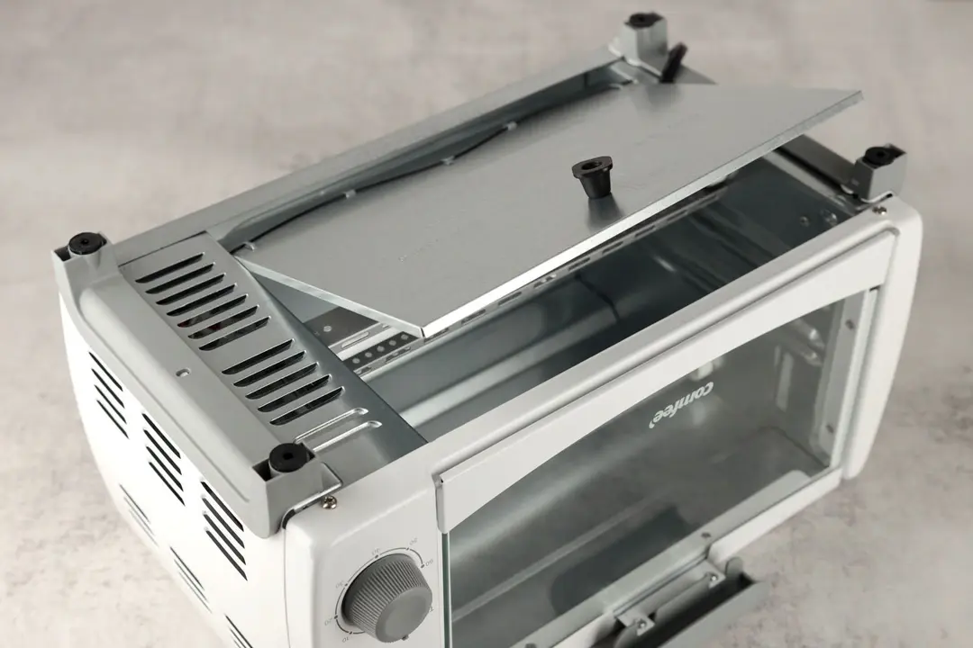 On a grey background, the bottom of the Comfee CFO-BB101 Toaster Oven has a detachable crumb tray, four stands, and holes.