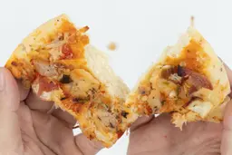 Two hands break apart a slice of pizza with cheese, meat, onions, and green bell peppers on top baked using a toaster oven.