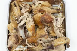 Eight pieces of a carved chicken including two carcass halves, two breasts, two wings, and two thighs on a baking pan.