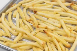 A close-up of pieces of baked french fries using the Panasonic NB-G110P Oven on a silver baking pan on a white background.