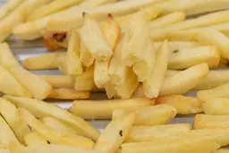 Twelve pieces of broken-up baked french fries are stacked on top of pieces of whole fries on a grooved silver baking pan.