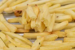 Twelve pieces of broken-up baked french fries are stacked on top of pieces of whole fries on a grooved silver baking pan.