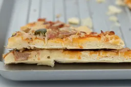 Two slices of toaster oven baked pizza on top of one another. It’s a 9-inch thick-crust meat pizza with cheese, onions, and green bell peppers on top. The pizza is inside a grooved silver baking pan.