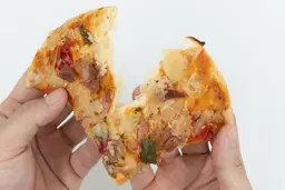 On a white background, two hands break apart a slice of baked pizza using a toaster oven with cheese, meat, and green bell peppers on top.