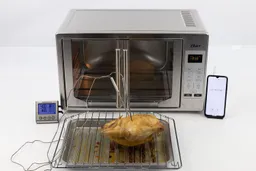 A whole chicken roasted using a toaster oven on a baking rack with a silver baking pan below. The thermometer displays the same temperature of 181°F from two probes inserted into the right and left thighs of the chicken.