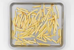 Pieces of baked french fries using a toaster oven inside a silver grooved baking pan on a white background.