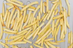 A closeup of pieces of baked french fries using a toaster oven inside a silver grooved baking pan.