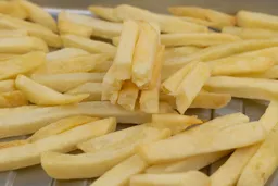 Pieces of baked french fries using a toaster oven. Eight pieces of broken-up fries are stacked on top of pieces of whole fries inside a silver grooved baking pan.