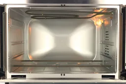 The cooking chamber of the Oster TSSTTVFDDG Toaster Oven has one nichrome heating element on top and two on the bottom, two rack levels, a shining light, and a fan cavity on the right wall.