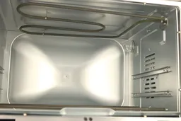 The cooking chamber of the Oster TSSTTVFDDG Toaster Oven has one bent nichrome heating element on top and two straight ones on the bottom, two rack levels, a light, and a fan cavity on the right wall.
