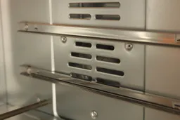 Two assembled guide rails on the right side of the Oster TSSTTVFDDG XL Digital French Door Convection Toaster Oven’s cooking chamber. A fan cavity is in between the two rails.