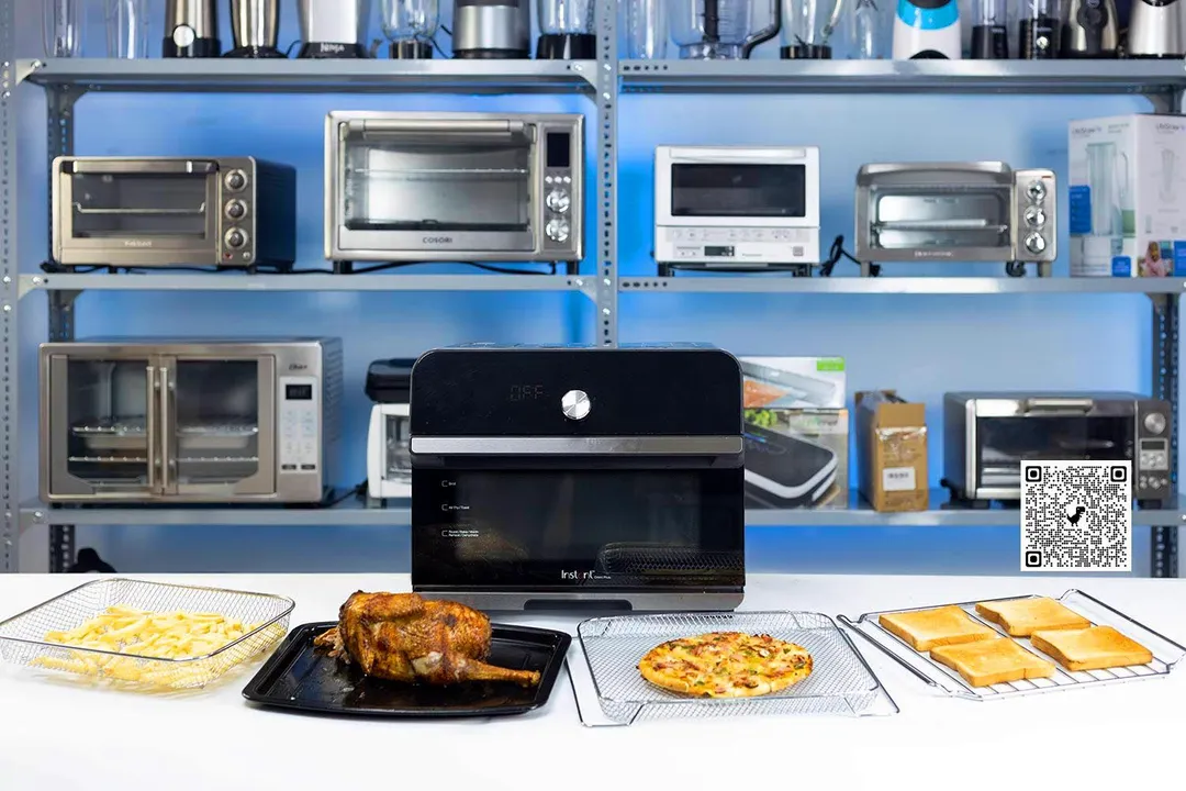 Toaster oven on a table with french fries, roasted chicken, pizza, and toasts in the front, other toaster ovens on a shelf at the back