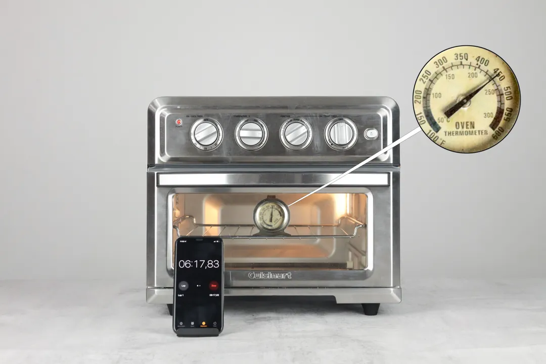 On a grey background, the Cuisinart TOA-60 Convection Air Fryer Toaster Oven with the interior light on. The oven thermometer inside says 450°F. The smartphone timer outside the oven says 6 minutes 17 seconds.