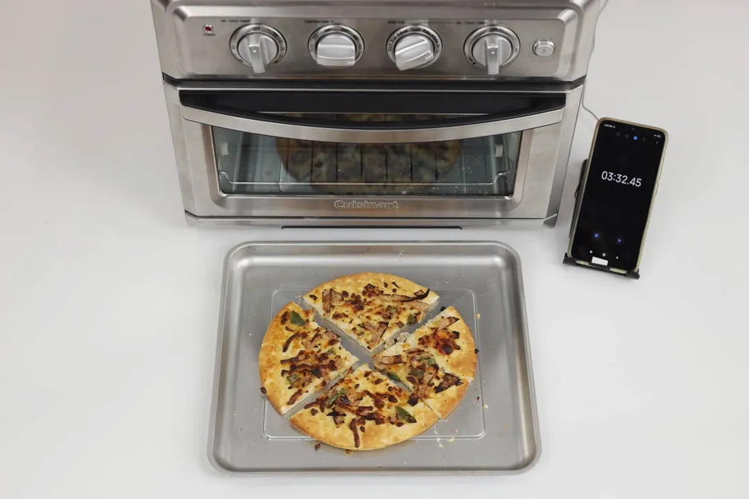 A 9-inch thick-crust meat pizza with cheese, onions, and green bell peppers on top baked with the Cuisinart Air Fryer Toaster Oven TOA-60 and cut into 4 slices. The pizza is inside a silver baking pan on a white background.