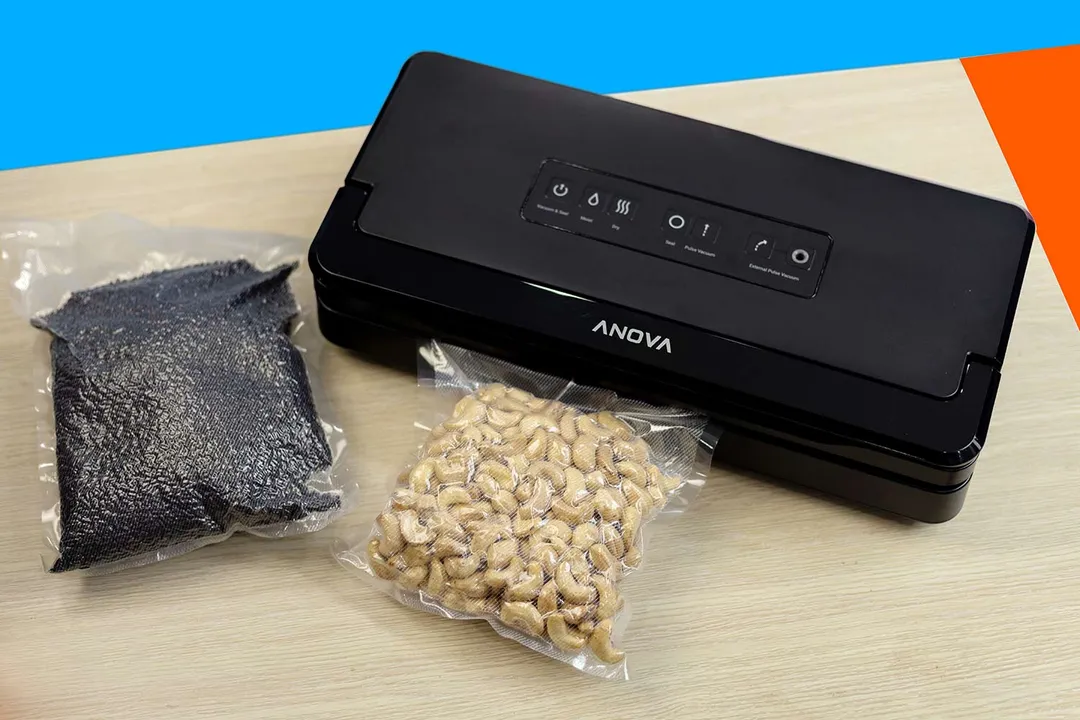 The black Anova Precision Pro vacuum sealer on a wooden surface. In front of it are vacuum bags containing roasted cashews and black rice grains.