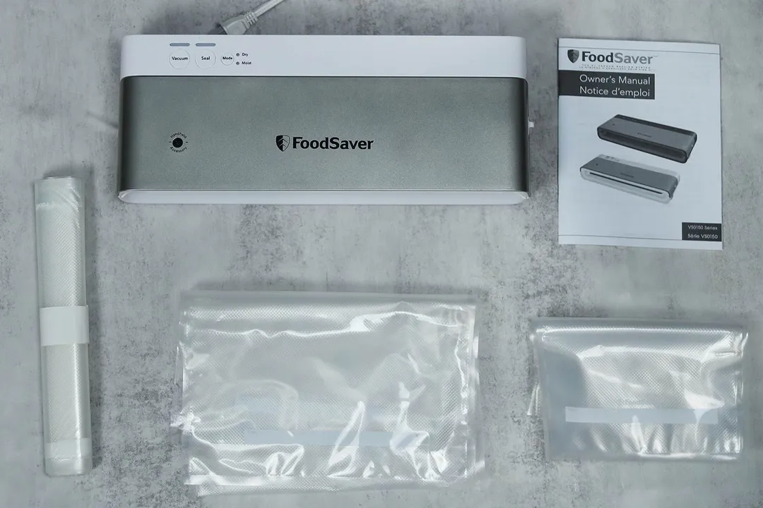 The content of the FoodSaver VS-0160 shipping box, consisting of the vacuum sealer, three rolls of food bags, and manual.