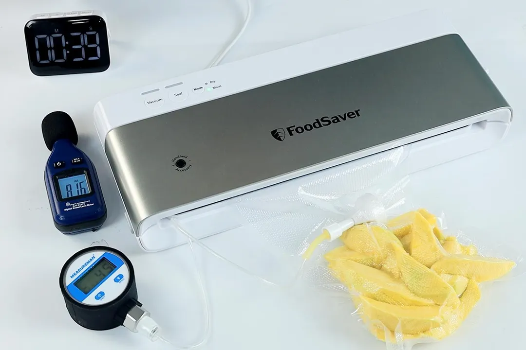 The FoodSaver VS0100 vacuum sealer vacuum-packaging a bag of yellow mango slices. To the left is a vacuum gauge reading 45 kPA.