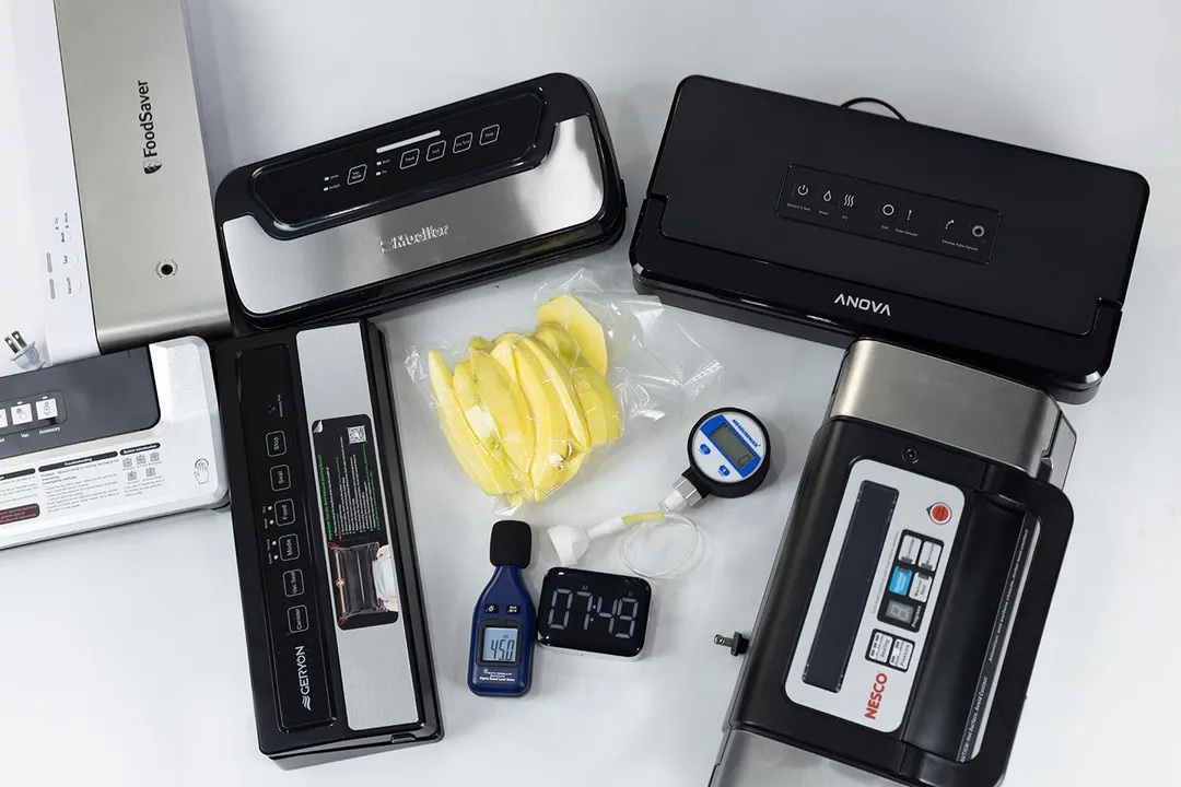 Vacuum sealers arranged around a bag of fresh fruit slices and testing instruments, which include a vacuum gauge, timer, and a noise level meter.