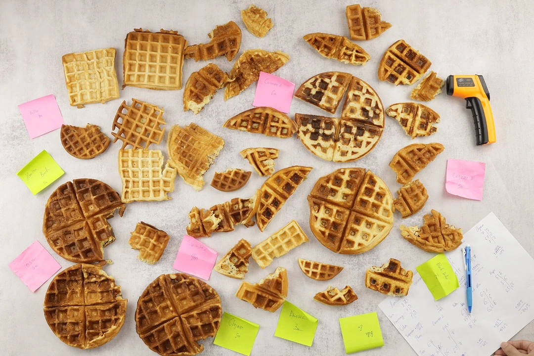 Many finished waffles laid on a table surrounded by Post-its and testing tools like thermometers and pens after a cooking test.
