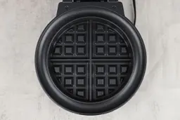 The black, Belgian-style waffle plate of the Chefman waffle maker. An anti-overflow moat surrounds it to catch excess batter.