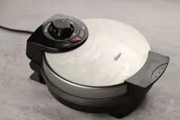 The side profile of the Oster CKSTWF2000 Belgian waffle maker. The stainless steel lid is blemished from daily use.