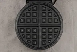 A close-up of the black, cast aluminum waffle plate of the Oster waffle maker.