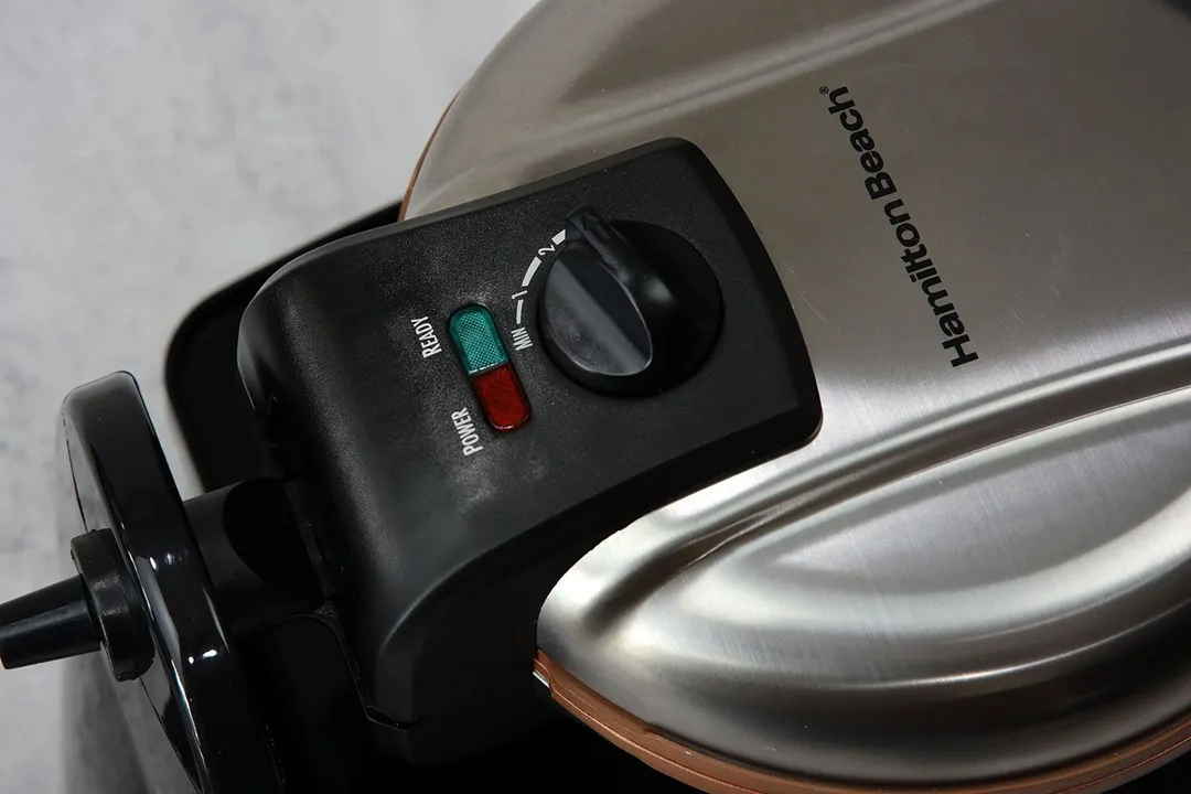 A close-up shot of the Hamilton Beach Belgian waffle maker (26031) control panel section made from black plastic, with the browning control knob and the indicator lights in focus.