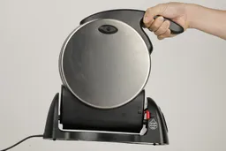 The entire Presto waffle maker is held in the air by the handle with one hand of a product tester.