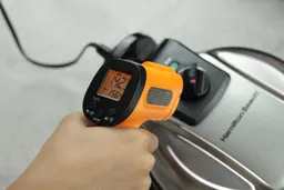 The temperature on the control panel of the Hamilton Beach 26031 is being measured using a thermometer during a thermal safety test. The display reads 142.3°F.