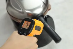 The temperature on the cool-touch handle of the Hamilton Beach 26031 is being measured using a thermometer during a thermal safety test. The display reads 90.3°F.