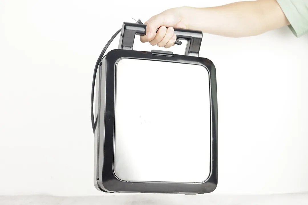 The KRUPS waffle maker being held in the air by its handle.