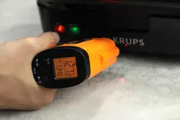 The temperature of the KRUPS waffle maker’s frontal control panel is being measured. The thermometer’s screen reads 127.2°F.