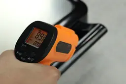 The temperature of the handle is being measured using a thermometer in a thermal safety test. The screen reads 89.8°F.