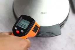 The temperature of the front handle of the Oster waffle maker is measured with a thermometer. The screen reads 189°F.