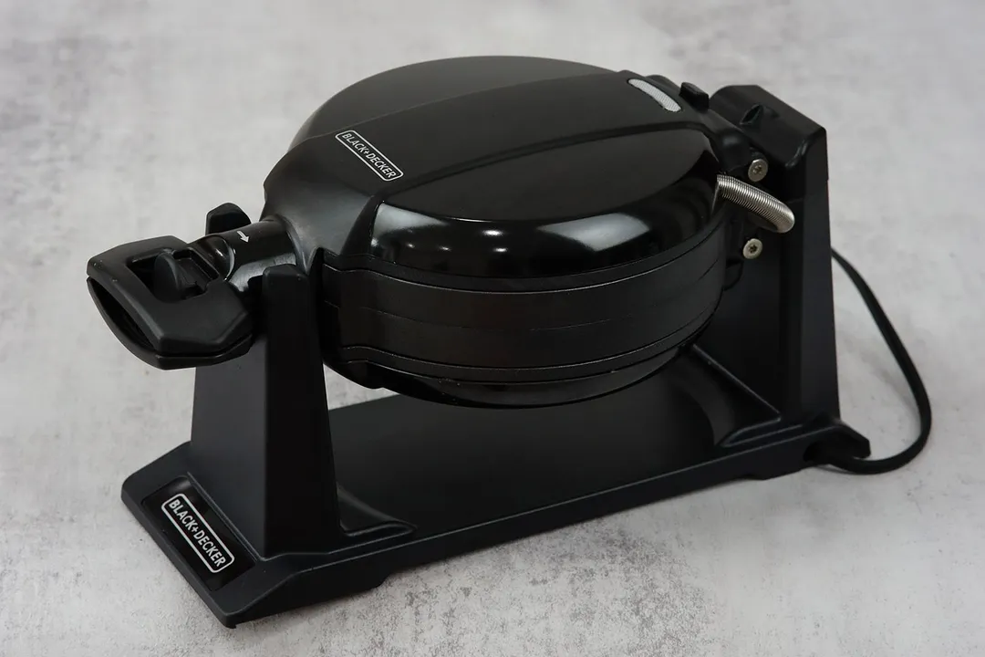 The side profile of a BLACK+DECKER WMD200B Belgian waffle maker, showcasing the machine’s all-black body made from smooth plastic.
