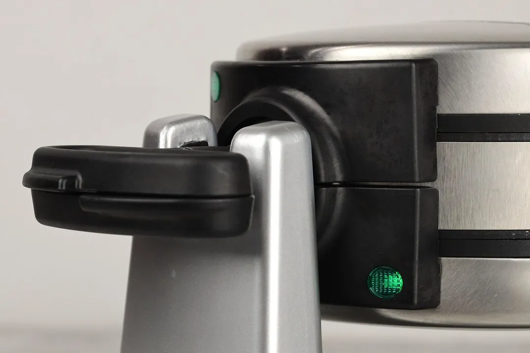 The front section of Cuisinart WAF-F20P1 double Belgian waffle maker with a rotating handle made from black plastic, green indicator light is on.