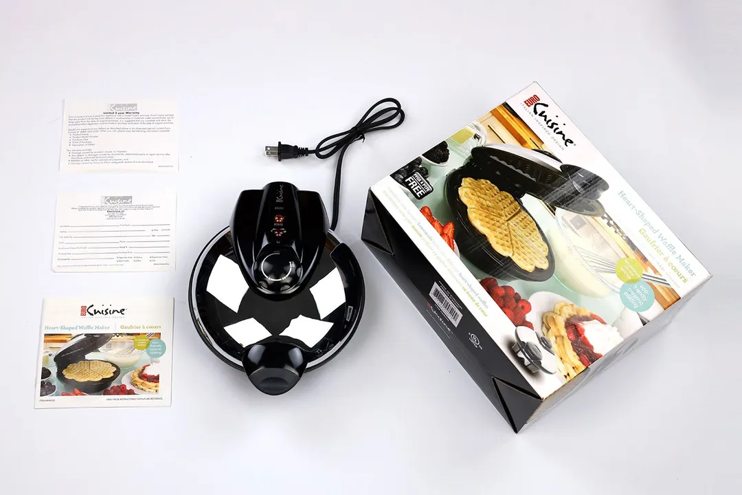 The Euro Cuisine Heart Shaped waffle maker is in the center. To its left is the manual and to its right is the shipping box.