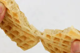 A waffle, baked for 5 minutes and 30 seconds, is torn up by hands to test its consistency. The waffle’s core can be seen.