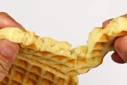The waffle is torn up by hand to test its consistency. The fluffy interior of the waffle is revealed.