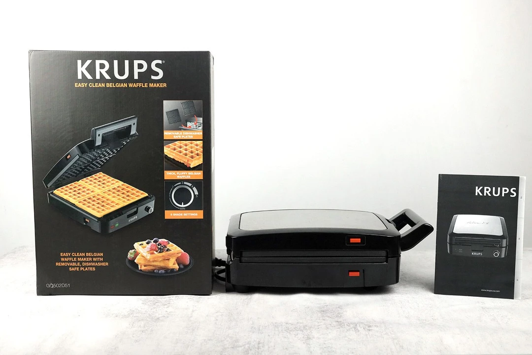 The side profile of the KRUPS Belgian waffle maker. To its left is the manual and to its right is the shipping box.