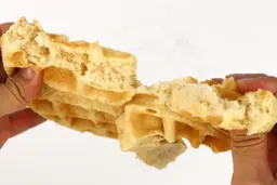A waffle being torn down the middle by hand to test its consistency and texture, revealing its golden interior.