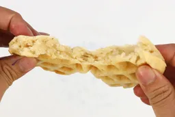 A waffle, baked for 8 minutes, being torn down the middle by hand to test its consistency, revealing the fluffy interior.