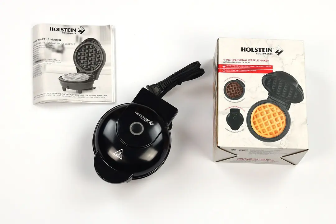 The glossy black Holstein 4 inch waffle maker next to its instruction manual and the shipping box.