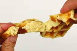 A waffle being torn by hand to test its consistency and texture. The interior of the waffle is revealed.