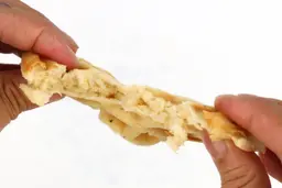 A waffle is torn down the middle by hands to test its consistency. The air bubble-filled interior of the waffle is revealed.