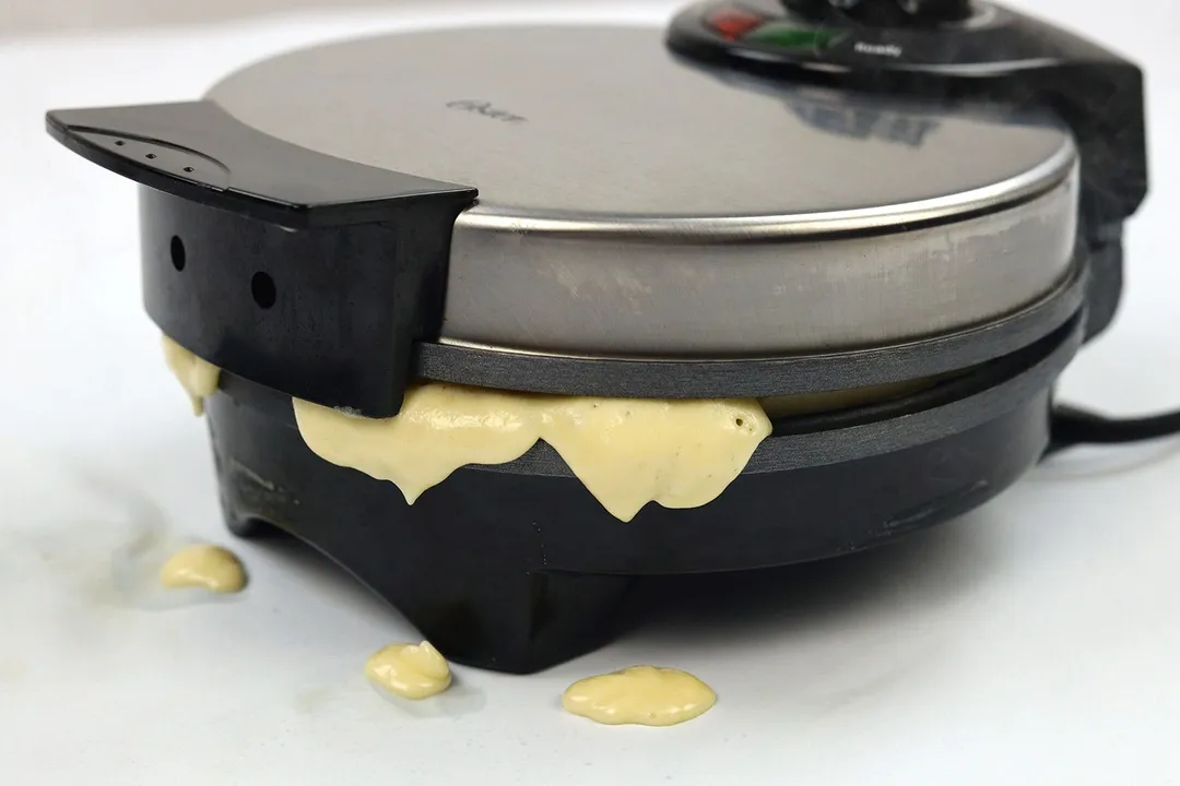Excess batter spilling out from the waffle plates of the Oster waffle maker.