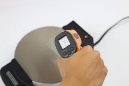 The surface temperature of the back of the Black and Decker WMB500 waffle maker is being measured with a thermometer during a thermal safety test. The screen reads 156°F.